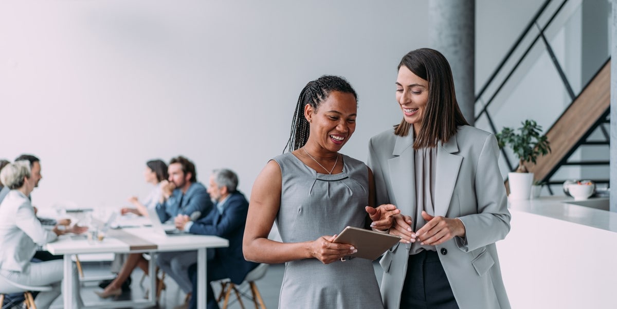 two professional women reviewing document in office, group of people sitting at a table inthe backrgound