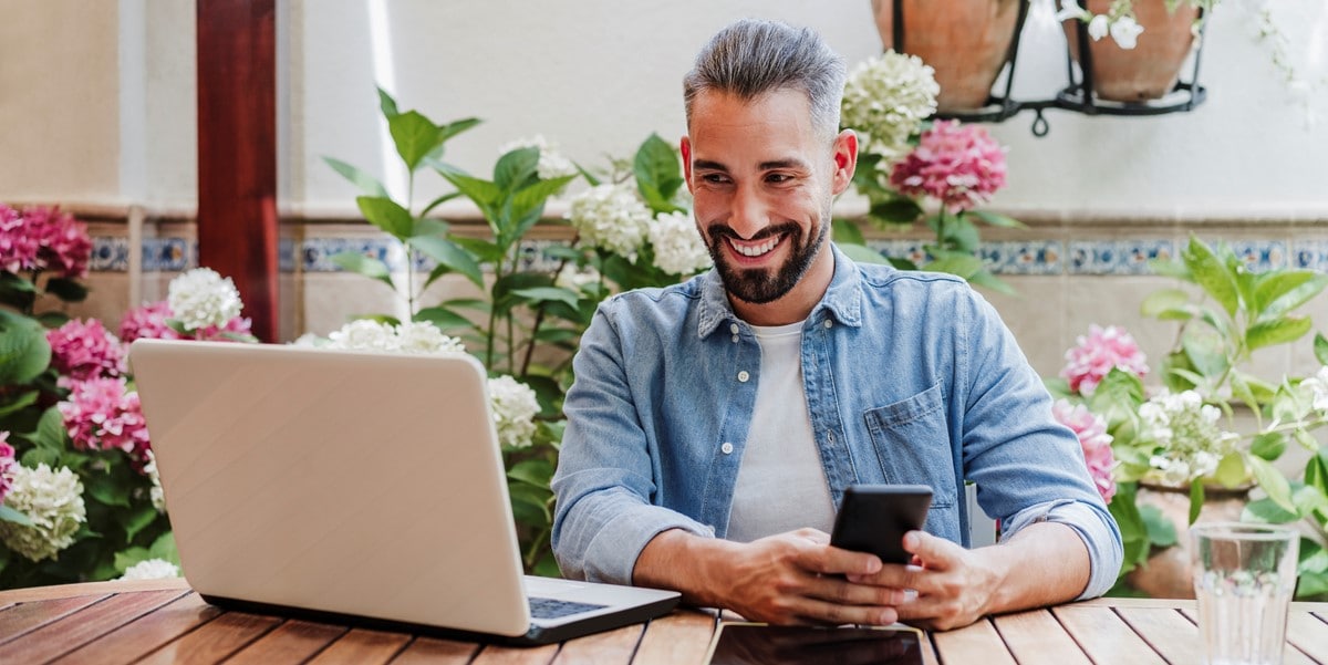 man working remotely, using cellphone and laptop at a table